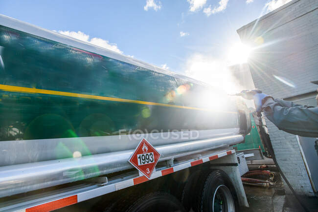 Worker pressure hosing biofuel oil tanker at sunlit biofuel plant — Stock Photo