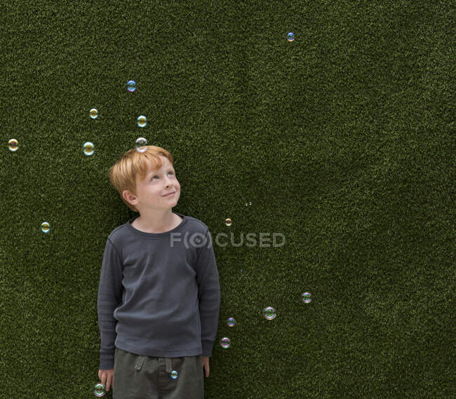 Хлопчик перед штучною травою посміхається на бульбашки — стокове фото