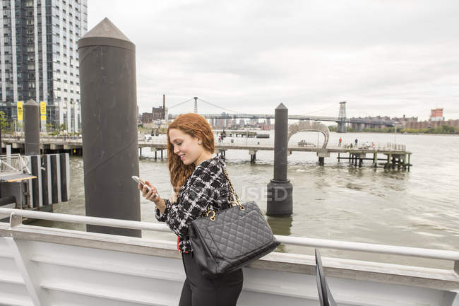 Joven mujer de negocios en la cubierta del ferry utilizando en el teléfono inteligente, Nueva York, EE.UU. - foto de stock