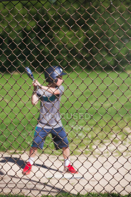 Vue à travers la clôture de fil de poulet de garçon jouant au baseball — Photo de stock