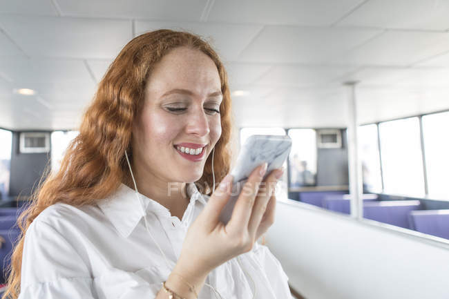 Mulher sorridente ouvindo música em fones de ouvido dentro de balsa de passageiros — Fotografia de Stock