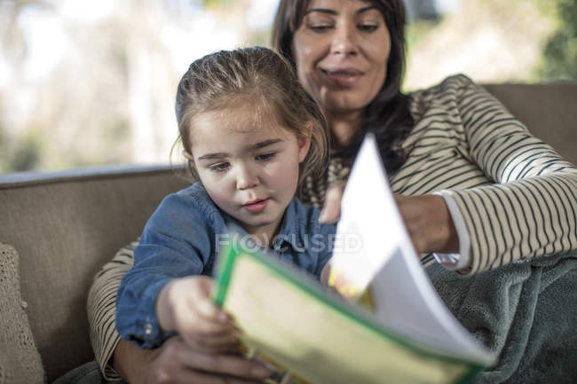Mature woman and daughter reading storybook on sofa — Stock Photo