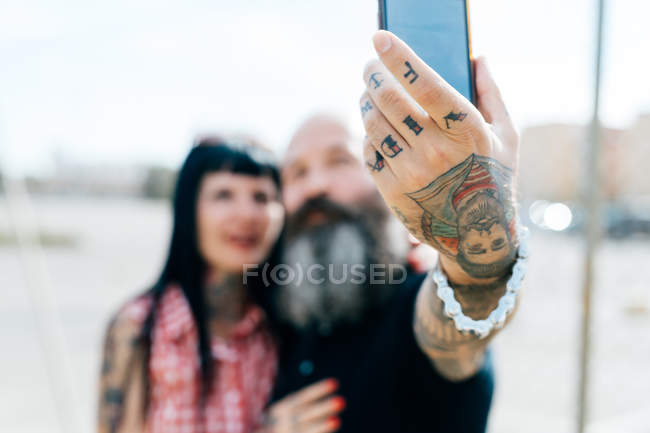 Mature tattooed hipster couple taking selfie, close up of hand — Stock Photo