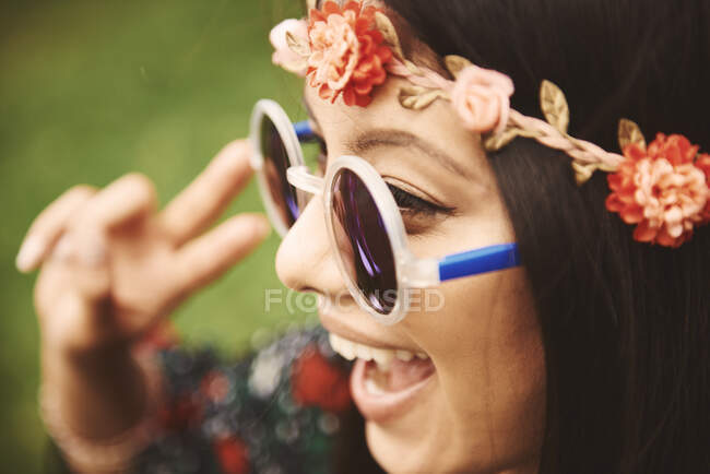 Mujer hippy joven en diadema floral haciendo signo de paz en el festival - foto de stock