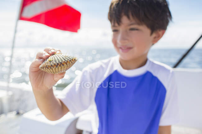 Boy examining scallop on boat, dive flag in background, Gulf of Mexico, Homosassa, Florida, US — Stock Photo