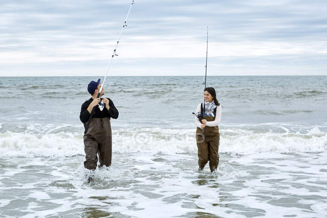 Молода пара в пивницях рибалка у воді — стокове фото