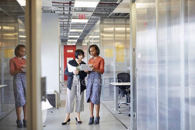 Две деловые женщины смотрят на цифровой планшет в офисном коридоре — стоковое фото