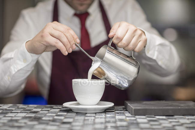 Waiter in restaurant, pouring milk into coffee cup, mid section — Stock Photo