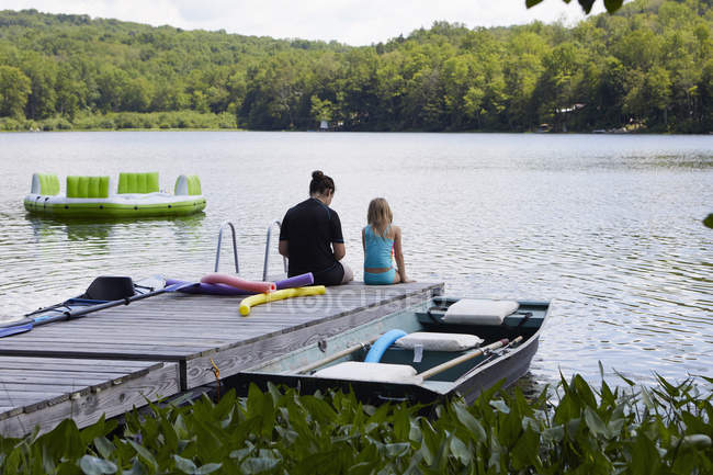 Due ragazze sedute sul molo accanto al lago — Foto stock