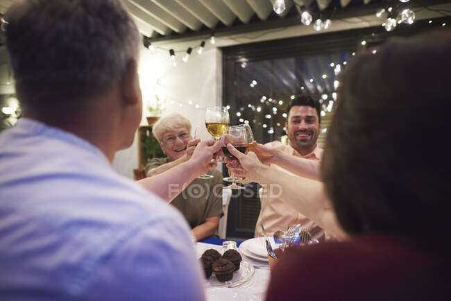 Gruppe von Menschen sitzt am Tisch, hält Weingläser in der Hand, prostet zu — Stockfoto