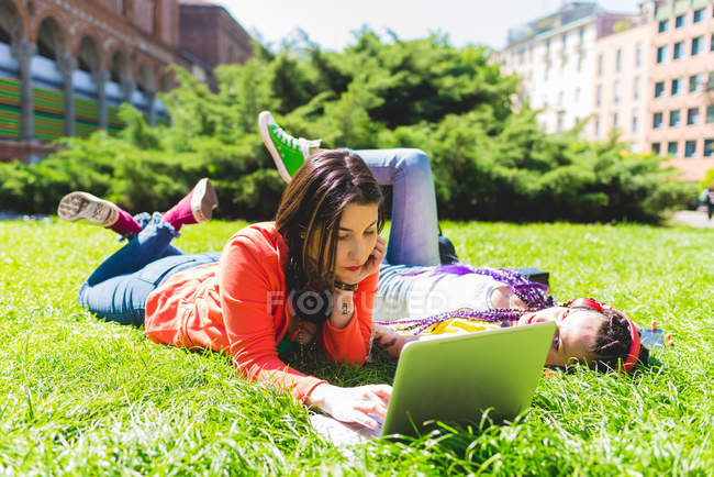 Mujer en el parque de la ciudad usando el ordenador portátil en la hierba, Milán, Italia - foto de stock