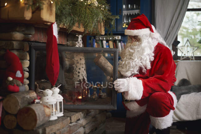 Santa Claus, indoors, putting log on fire — Stock Photo