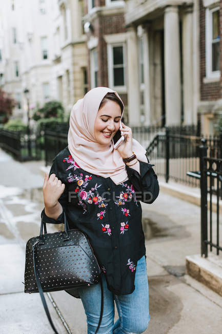 Mujer joven en hiyab haciendo una llamada telefónica en la calle - foto de stock