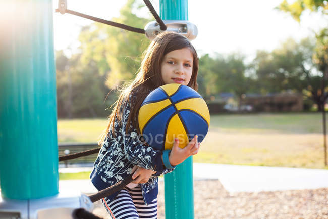 Девушка держит баскетбол на детской площадке и улыбается в камеру — стоковое фото