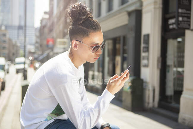 Молодой человек сидит на улице, используя смартфон — стоковое фото
