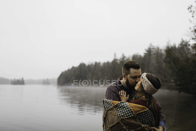Couple wrapped in blanket kissing near lake, Bancroft, Canada, North America — Stock Photo