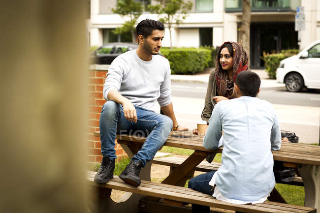 Amigos disfrutando del café juntos en el banco del parque - foto de stock