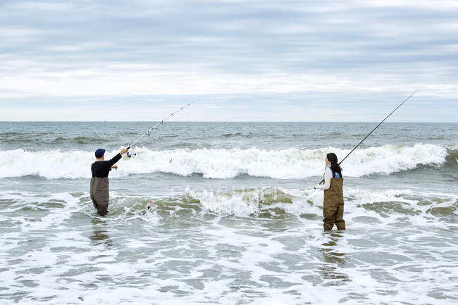 Young couple in waders casting off fishing rods — Stock Photo