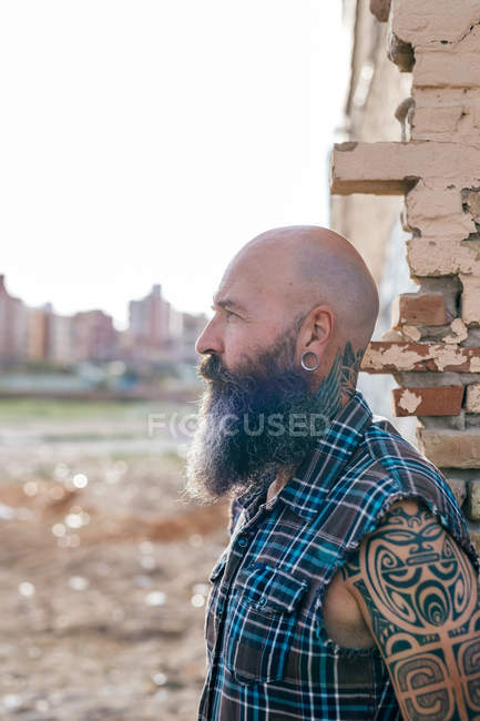 Tattooed mature male hipster by wall of demolished building — Stock Photo