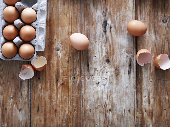 Яйця в яєчній коробці і розбиті мушлі на дерев'яній поверхні, вид зверху — стокове фото