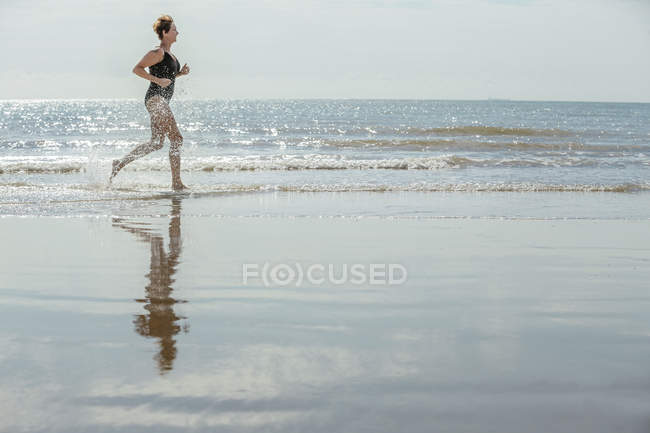 Вид збоку зрілої жінки, що біжить на пляжі — стокове фото