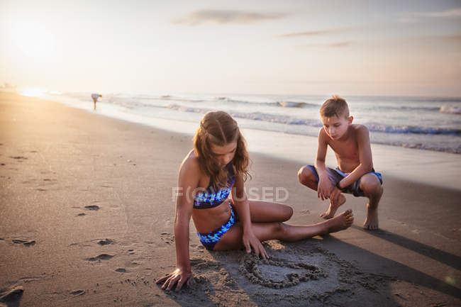 Fille avec garçon dessin coeur dans le sable sur la plage — Photo de stock