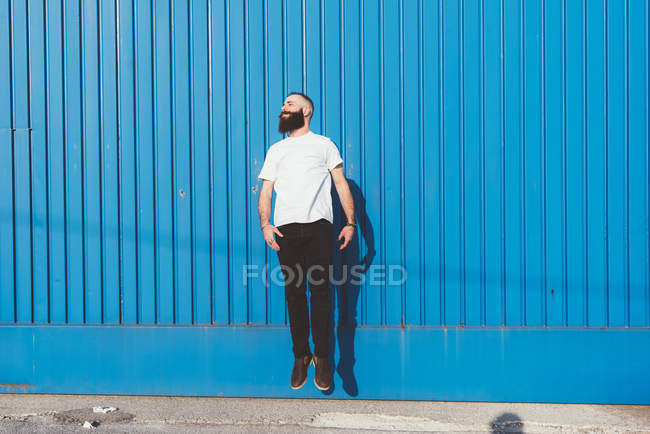 Бородатий чоловік перед синьою стіною стрибає в повітрі — стокове фото