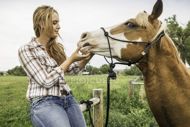 Jovem mulher olhando para a boca do cavalo no campo de fazenda, Bridger, Montana, EUA — Fotografia de Stock