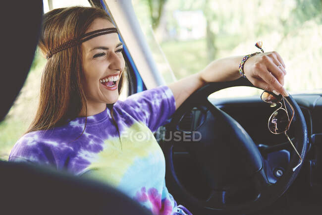 Joven mujer boho riendo en el asiento delantero de la furgoneta recreativa - foto de stock