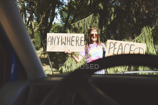 Car window view of young female boho hitchhiker with peace sign — Stock Photo