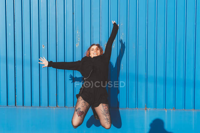 Femme devant le mur bleu sautant dans les airs — Photo de stock