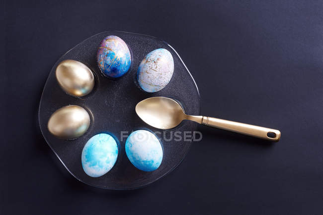 Vista aérea de huevos de Pascua pintados y teñidos de oro en plato con cuchara de oro - foto de stock