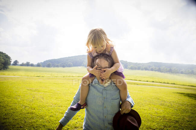 Menina ficando porquinho de volta de pai no campo rural, cobrindo seus olhos — Fotografia de Stock