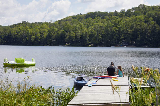 Rear view of two girls sitting on jetty beside lake — Stock Photo