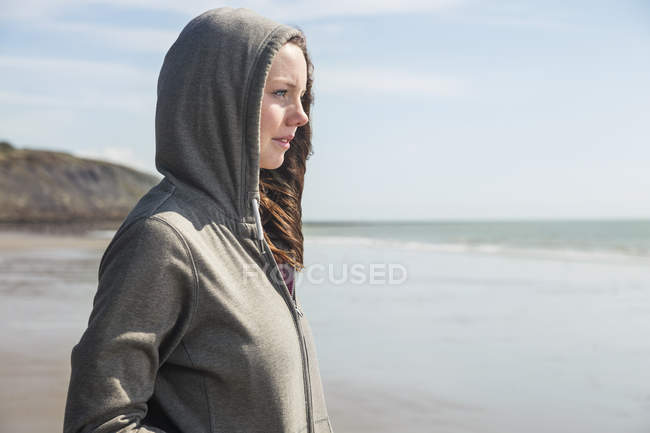Mujer joven con capucha superior mirando hacia la playa - foto de stock