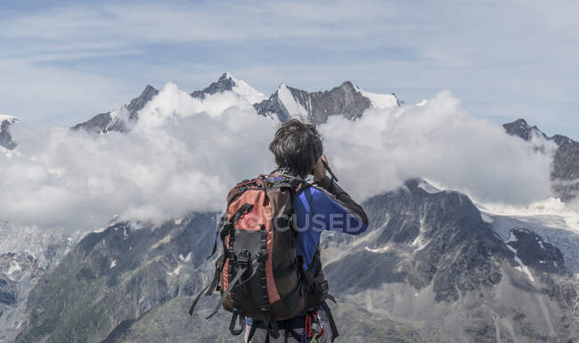 Rear view of male climber photographing low mountain clouds at Jegihorn, Valais, Switzerland — Stock Photo