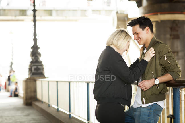 Giovane coppia in piedi faccia a faccia e ridere sotto il ponte — Foto stock
