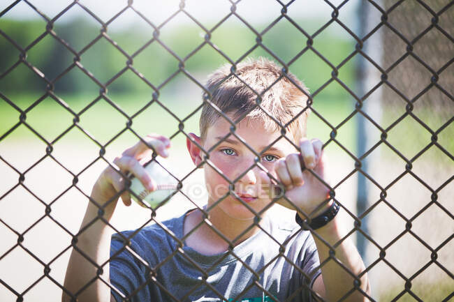 Vue à travers la clôture de fil de poulet du garçon regardant la caméra — Photo de stock