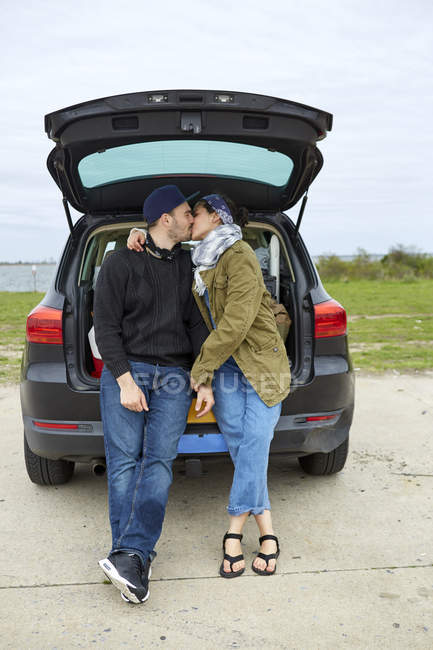 Young couple sitting and kissing in open car trunk — Stock Photo