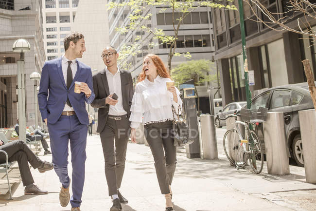 Young businesswoman and businessmen with takeaway coffee strolling along sidewalk — Stock Photo