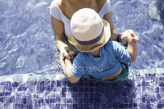 Mother and young son in outdoor swimming pool, elevated view, mid section — Stock Photo