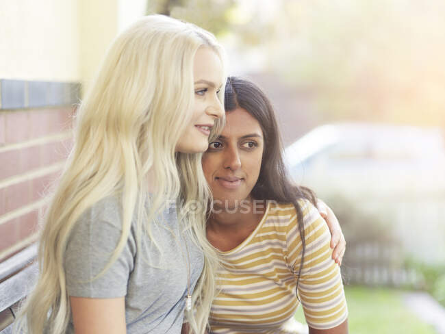 Young woman sitting on bench, hugging friend sitting beside her — Stock Photo