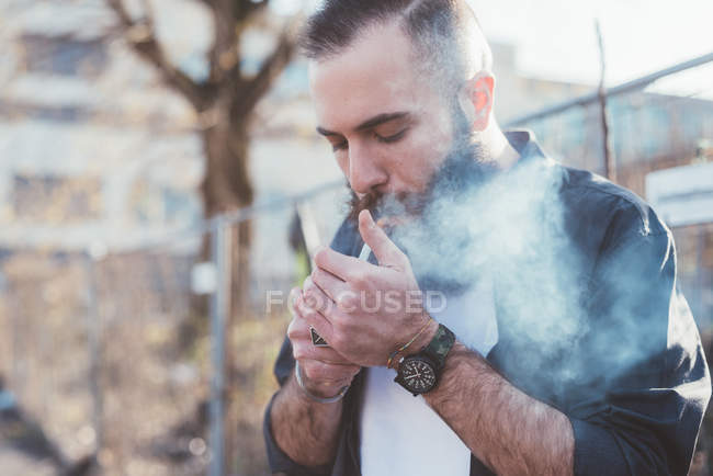 Молодой бородатый мужчина курит сигарету — стоковое фото