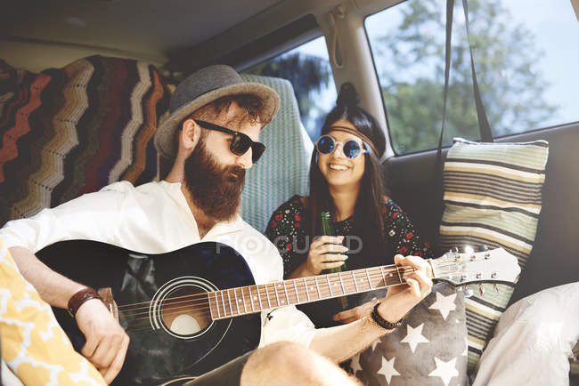 Jovem boho casal tocando guitarra acústica em van recreativa — Fotografia de Stock
