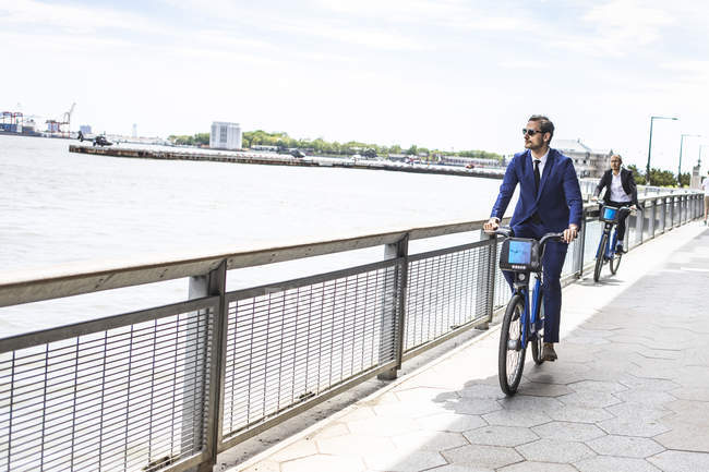 Dos hombres de negocios en bicicleta en el camino frente al mar - foto de stock