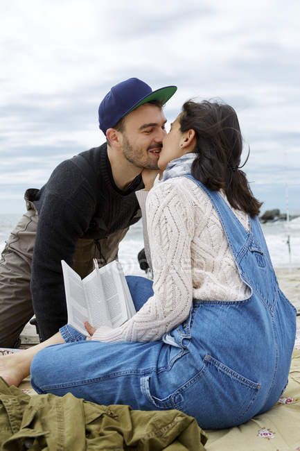 Young woman kissing sea fishing boyfriend on beach — Stock Photo