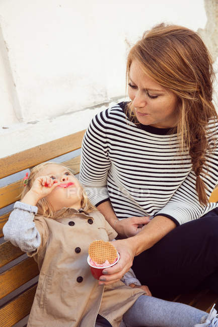 Mãe e filha de criança comendo sorvete no banco do parque — Fotografia de Stock