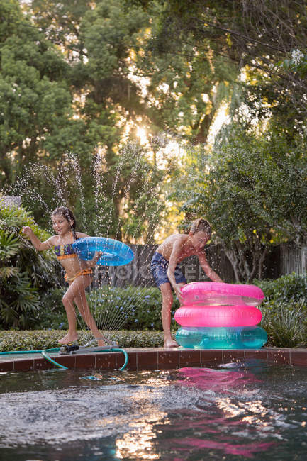 Jovem e menino se divertindo com anéis infláveis na piscina exterior — Fotografia de Stock