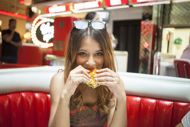 Porträt einer jungen Frau, die im Abendessen sitzt und Sandwich isst — Stockfoto