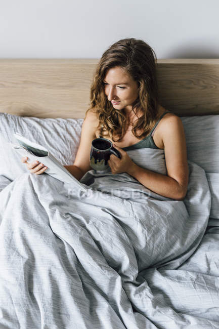 Молода жінка читає журнал в ліжку — стокове фото
